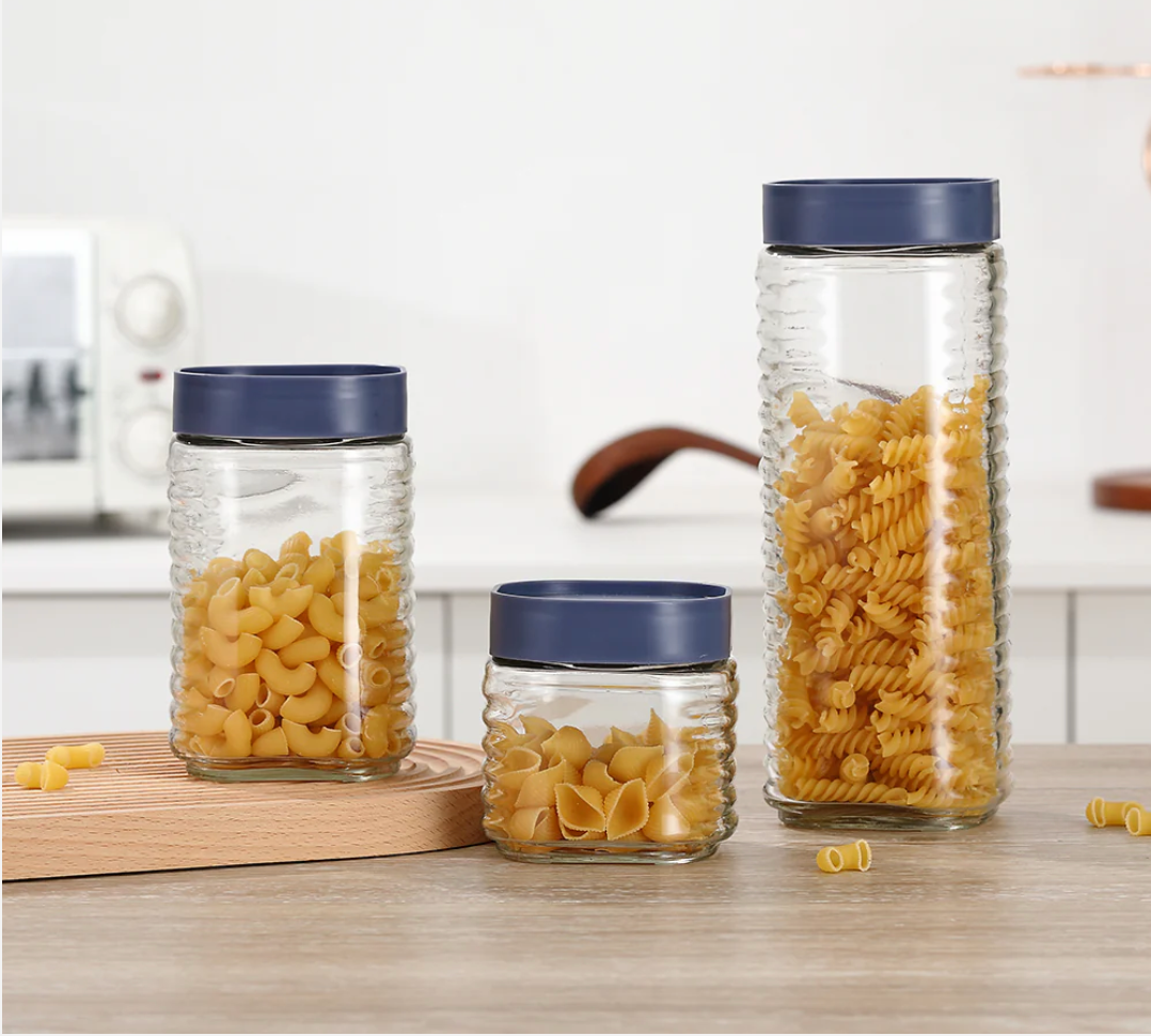 Glass jars with blue lids containing pasta on a kitchen counter.