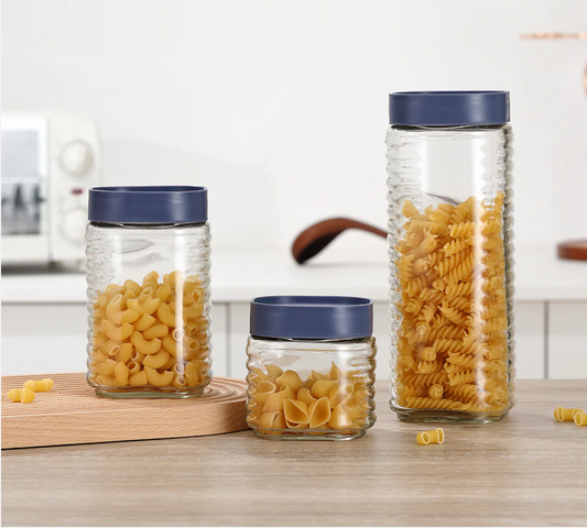Glass jars with blue lids containing pasta on a kitchen counter.